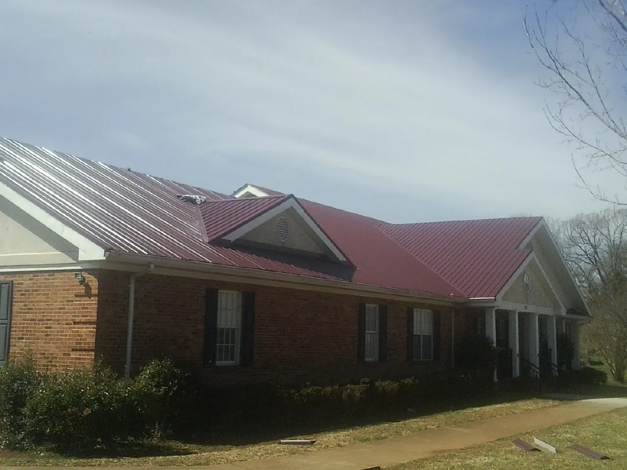 Red metal roof with gabled entries on a long brick building, from a Hail Damage Roof Repair job in Flagstaff