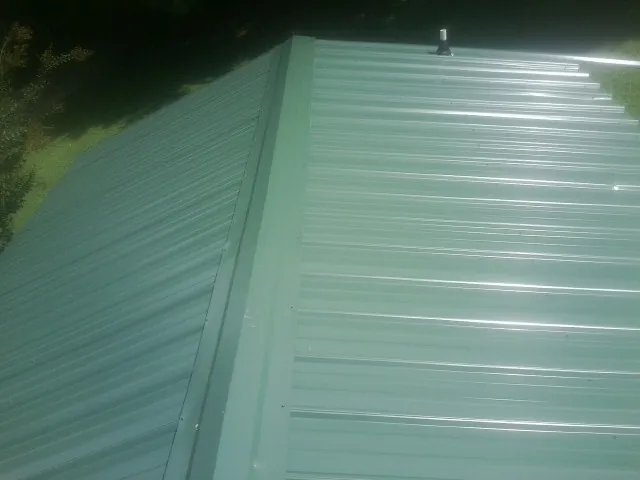 New green metal panels meeting at the ridge of a roof — Flat Roof Repair work by our crew in Flagstaff