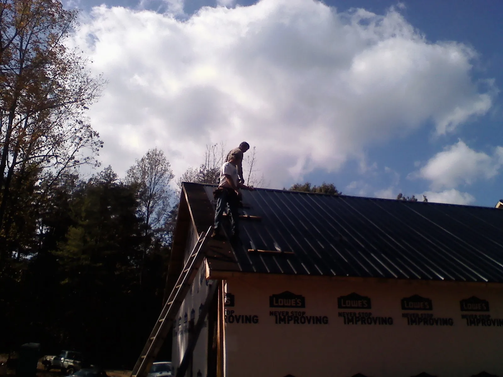 Roofer fastening dark metal panels high against a cloudy sky, from a Roof Inspection job in Flagstaff